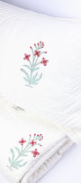 Folded luxury bedspread with floral block print and matching pillow cover on a white background