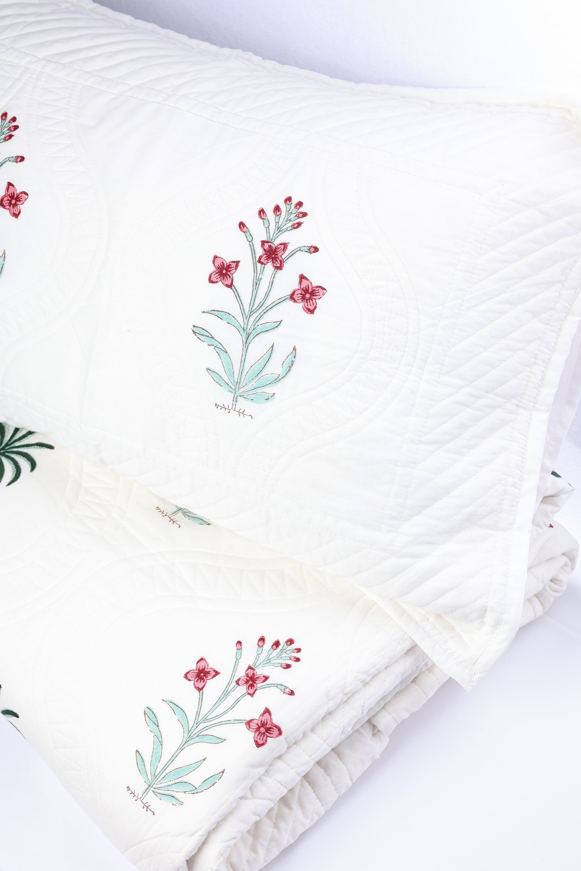 Folded luxury bedspread with floral block print and matching pillow cover on a white background