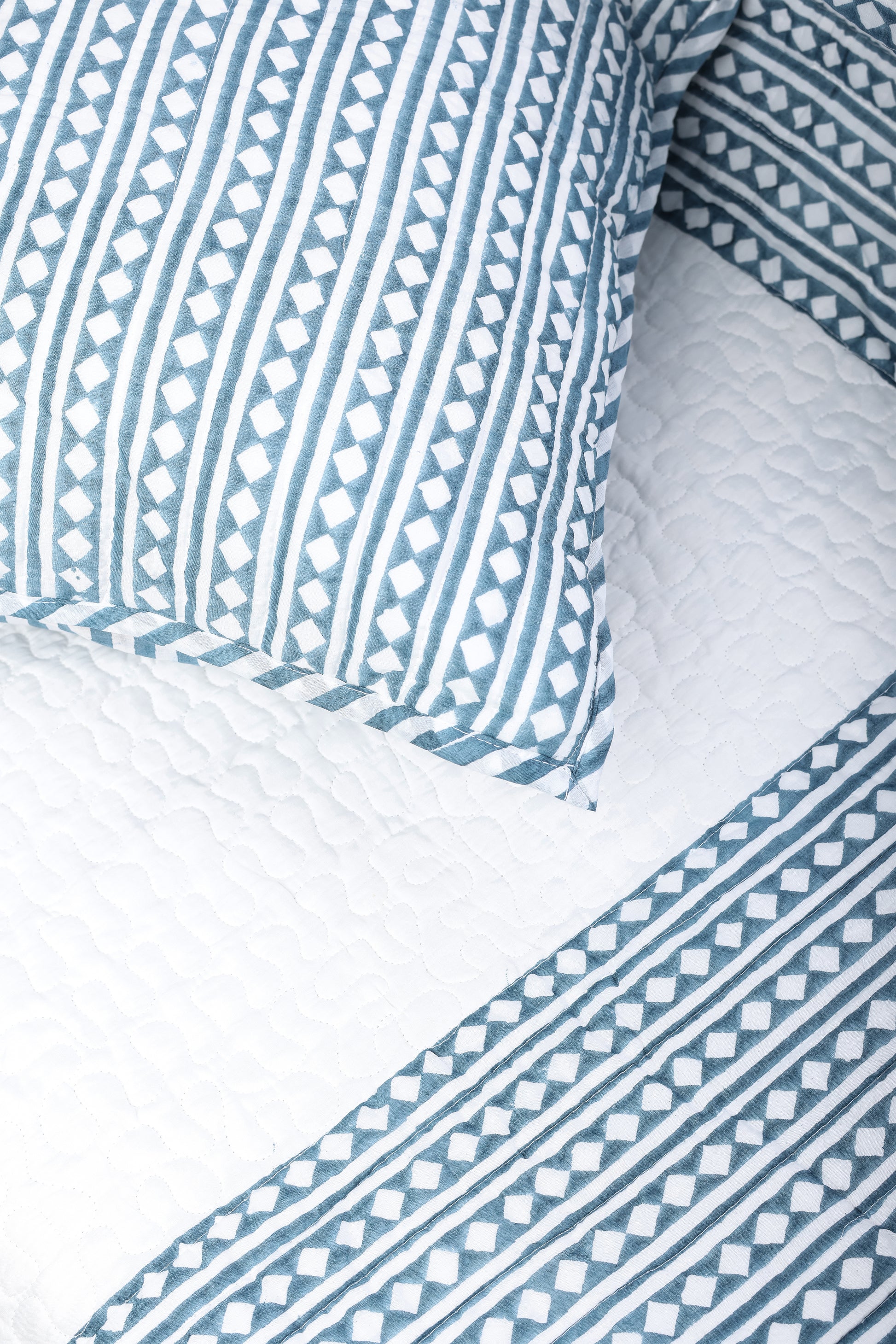 Close-up of blue and white quilted bed cover with matching cotton pillow cover. Buy luxry bedspread online.