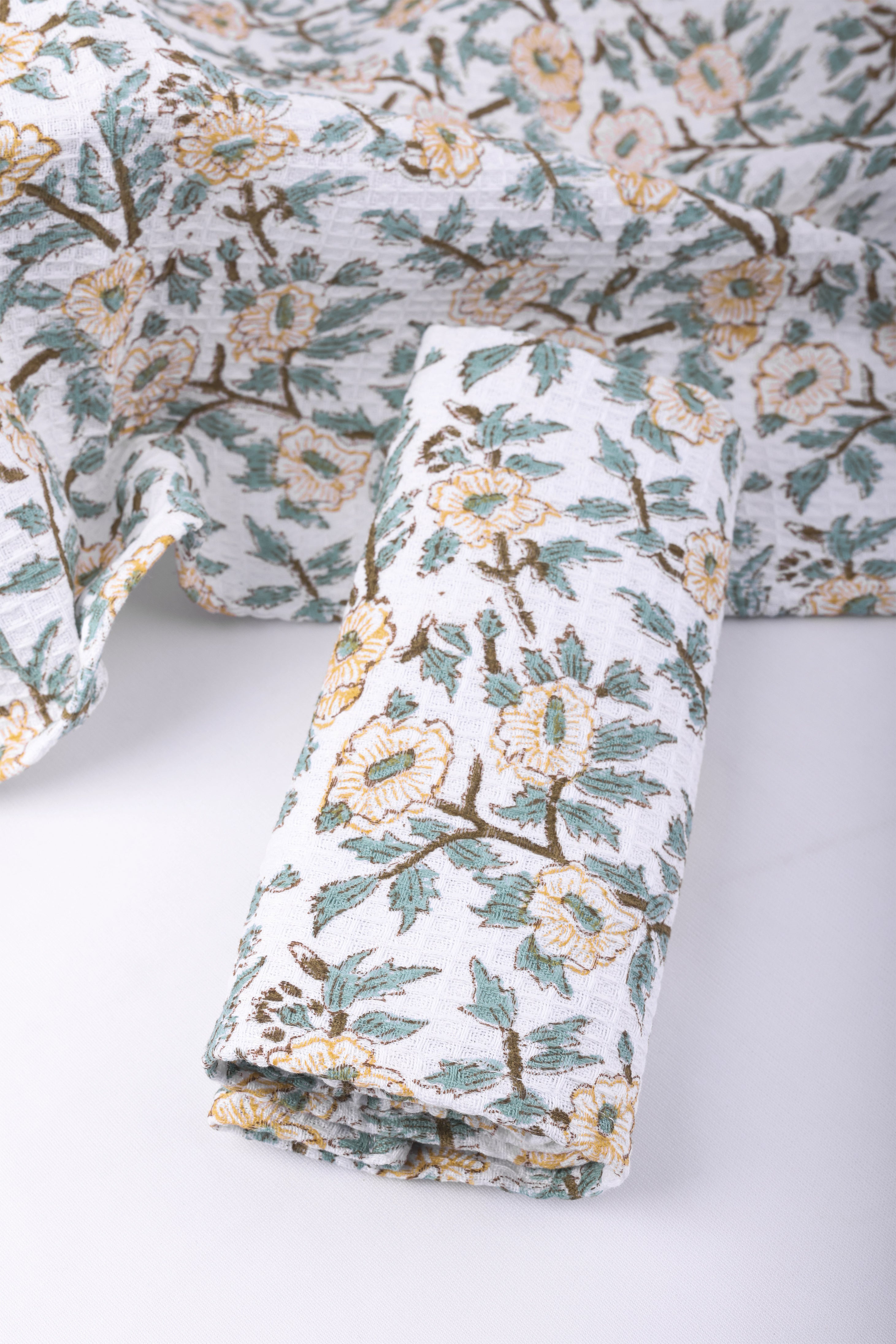 Folded floral cotton hand towels with green and yellow print on a white background. Buy bath linen online.
