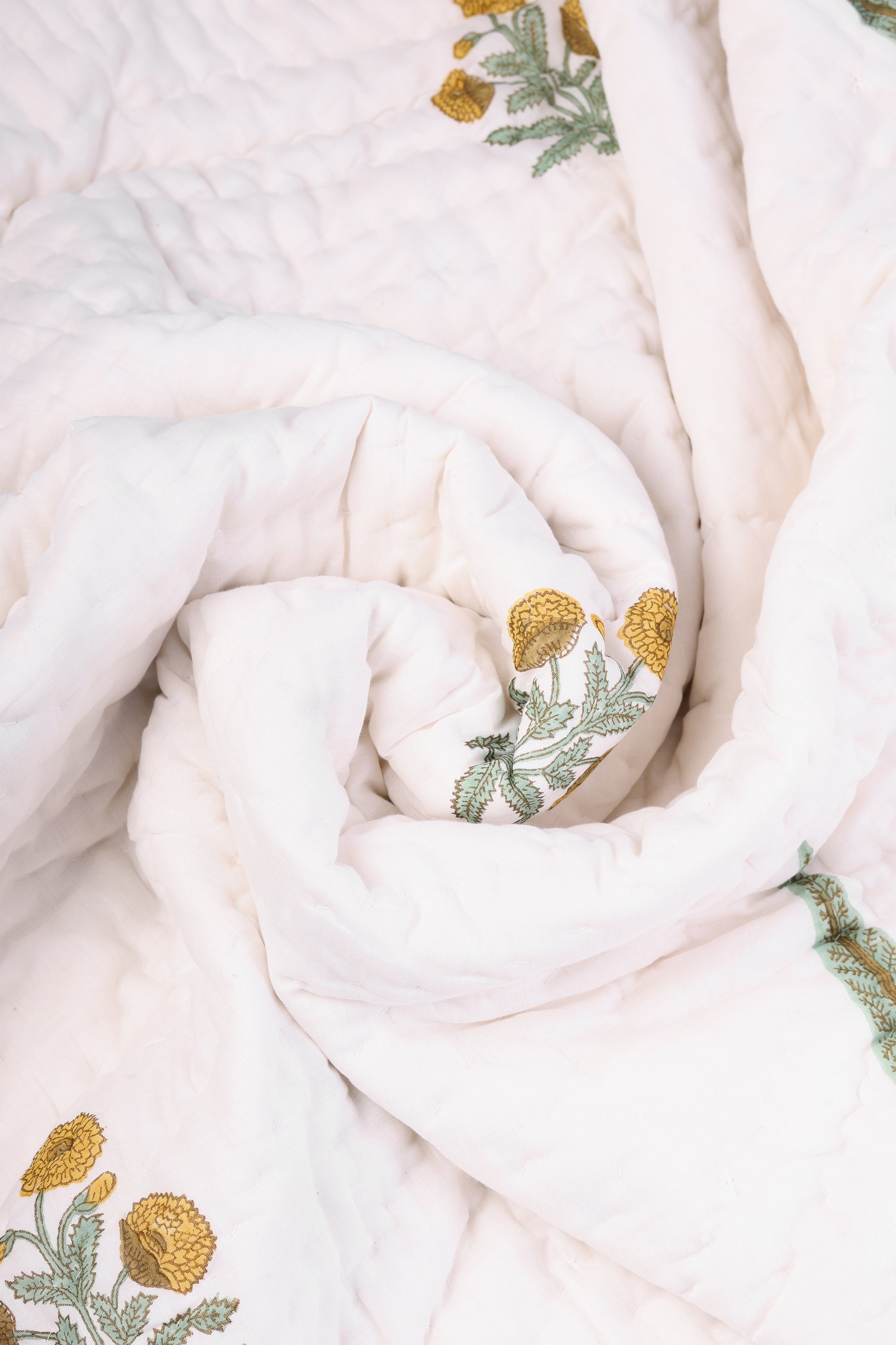 Folded white jaipuri razai with handblock yellow flowers and green leaves. Buy ac quilts online.