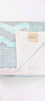 Folded reversible summer blanket with chevron and striped blue pattern on a white cloth