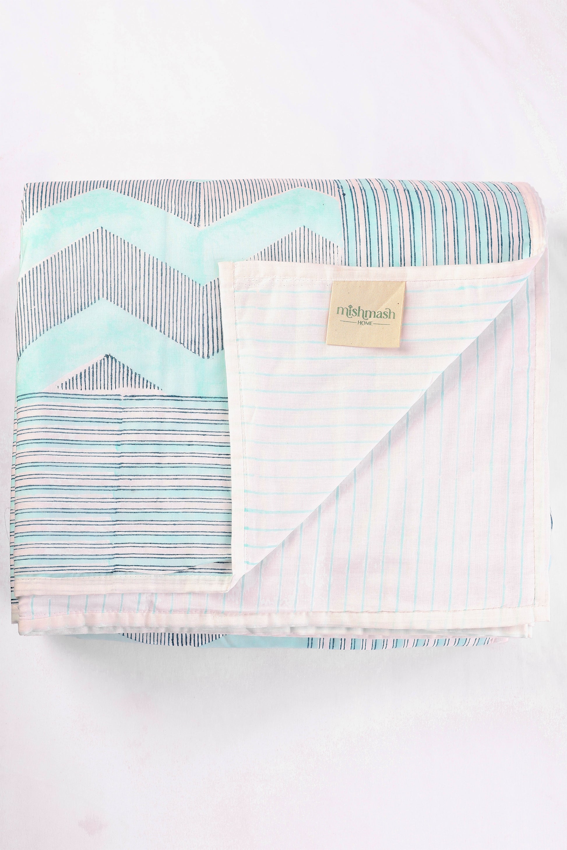 Folded reversible summer blanket with chevron and striped blue pattern on a white cloth