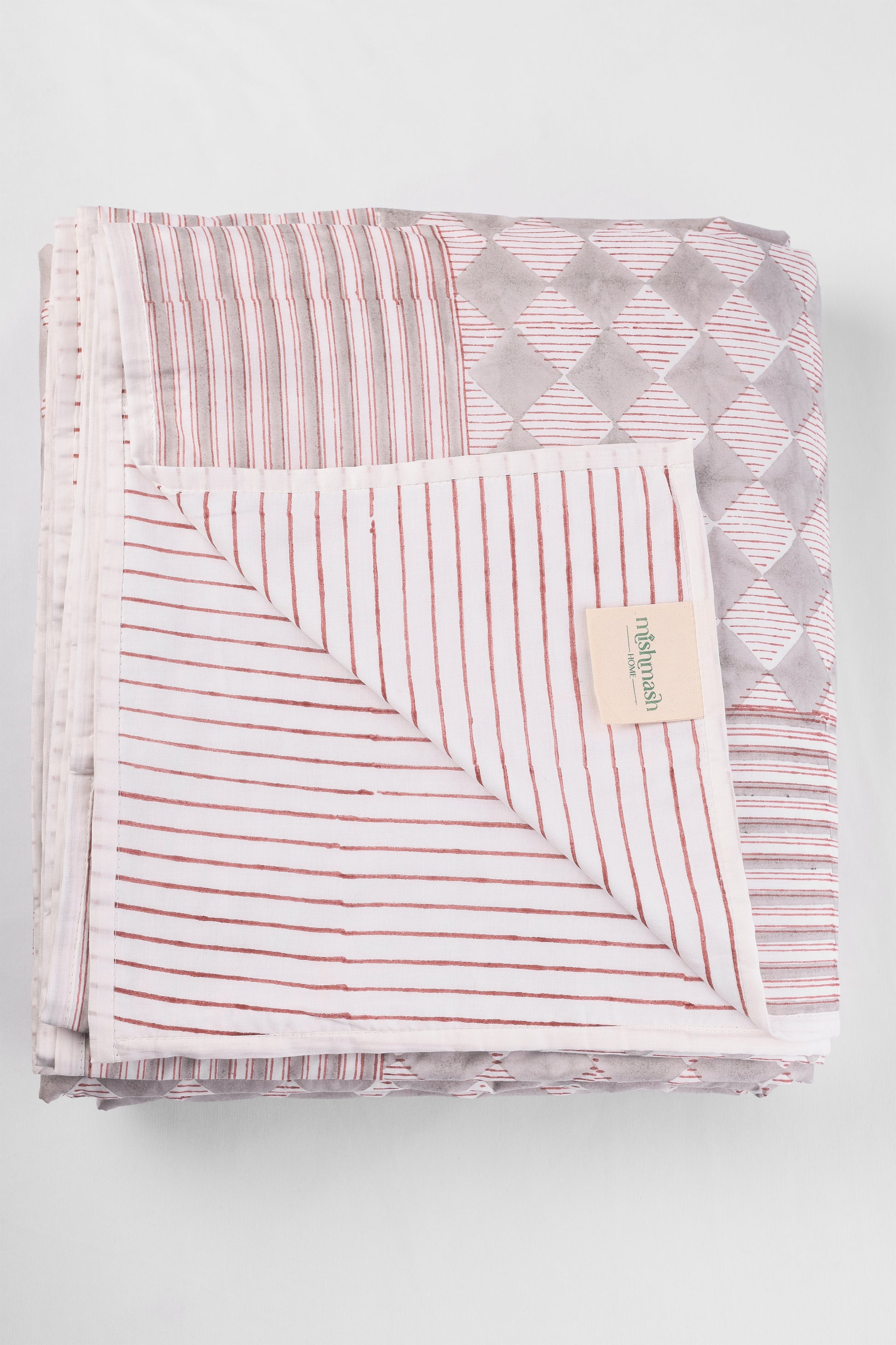 Folded reversible cotton dohar blanket with red striped pattern on a light gray background