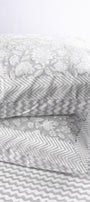 Two gray and white reversible cotton pillows on a light gray chevron print cotton double bed sheet