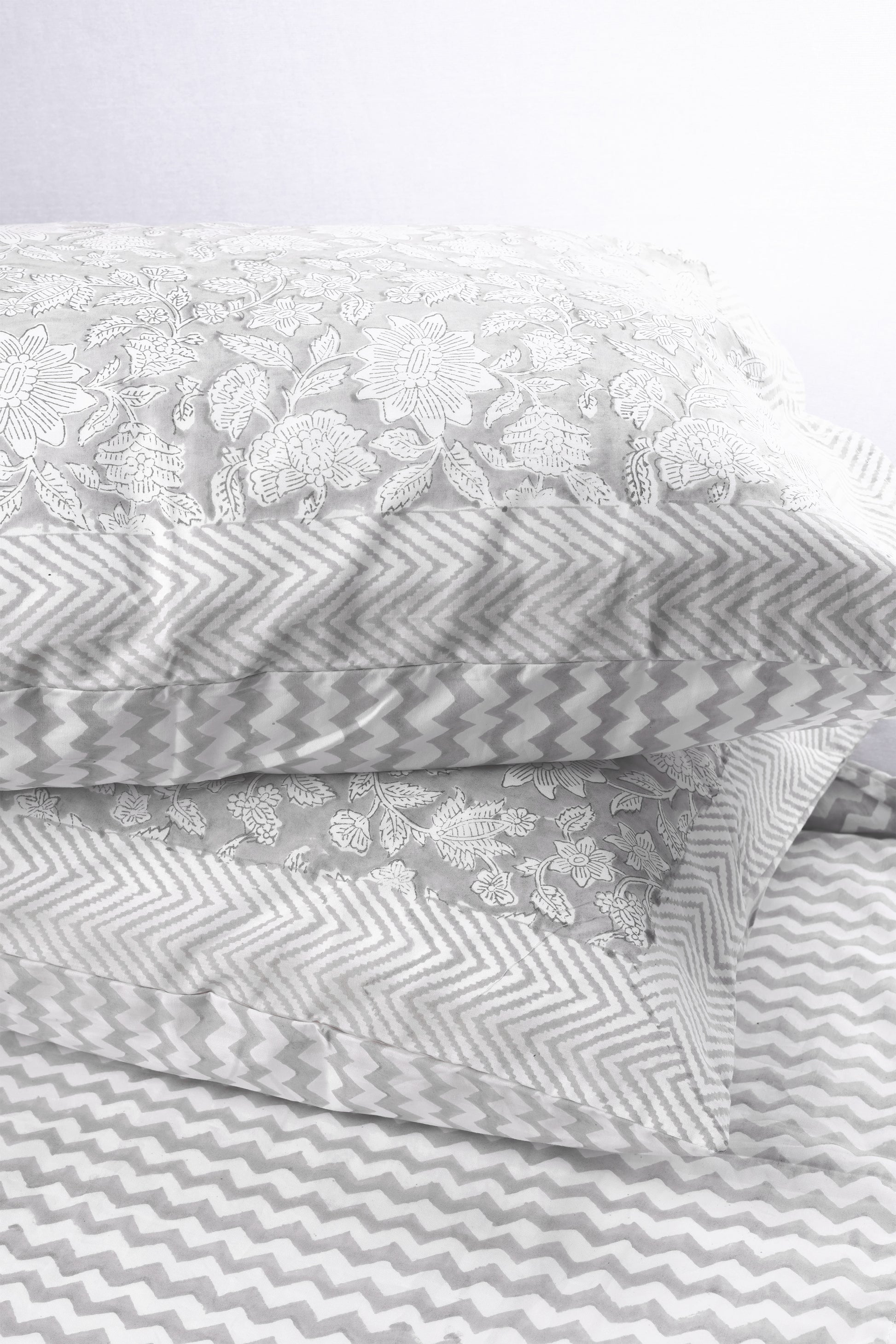 Two gray and white reversible cotton pillows on a light gray chevron print cotton double bed sheet