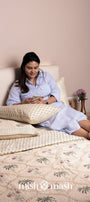 Woman sitting on a bed with pure cotton bed cover with floral motifs and two matching pillows, using a phone.