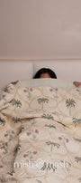 Person lying under a floral luxury bed spread in light yellow color with palm tree and floral motifs