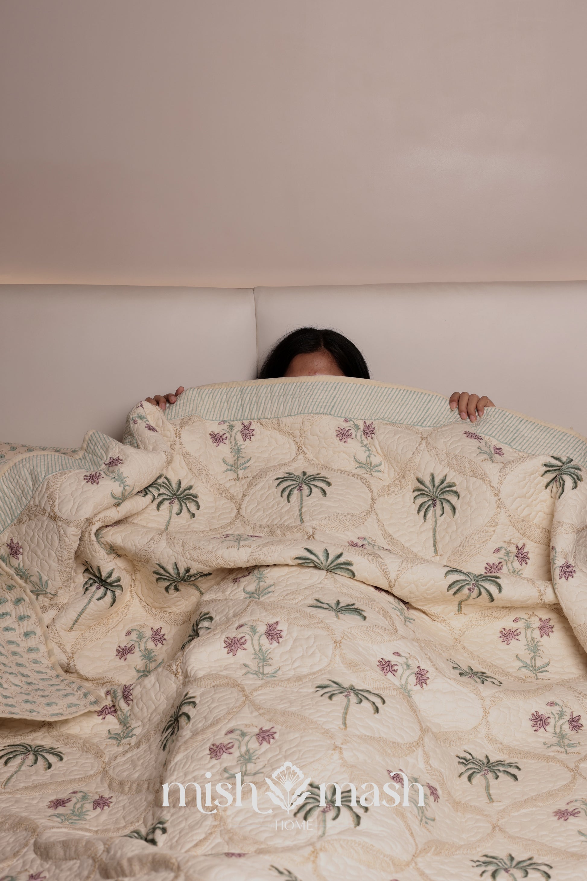 Person lying under a floral luxury bed spread in light yellow color with palm tree and floral motifs