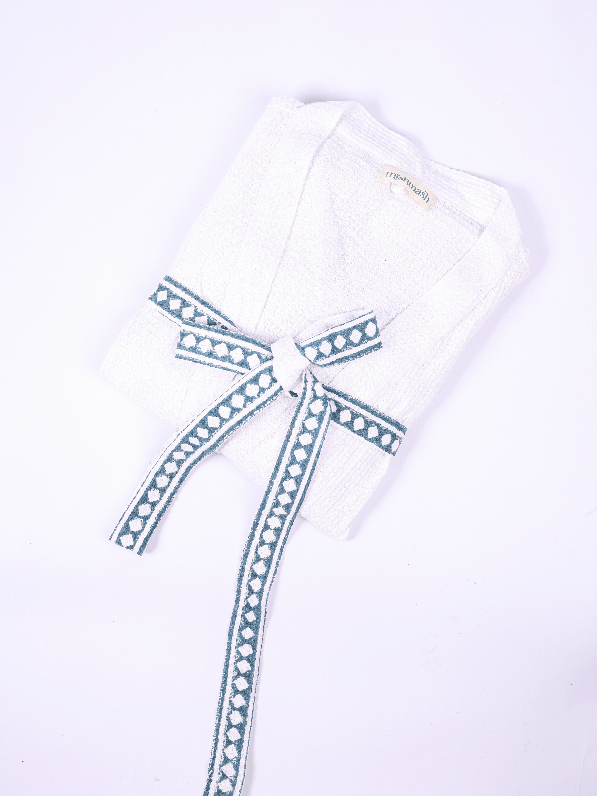 A folded white cotton robe with a long tie belt featuring a blue and white geometric pattern