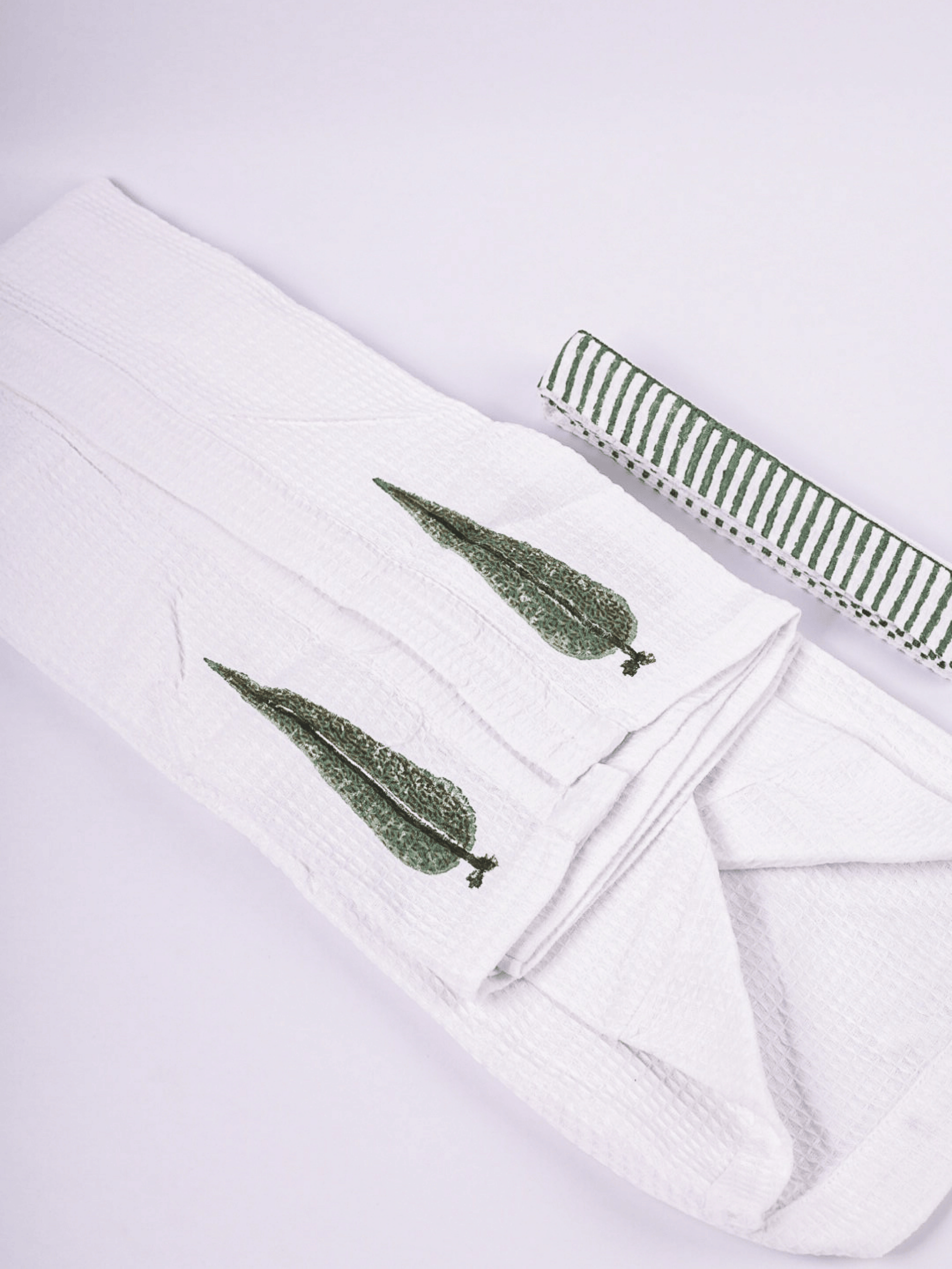 A folded white bathrobe with two green hand block printed leaf motifs